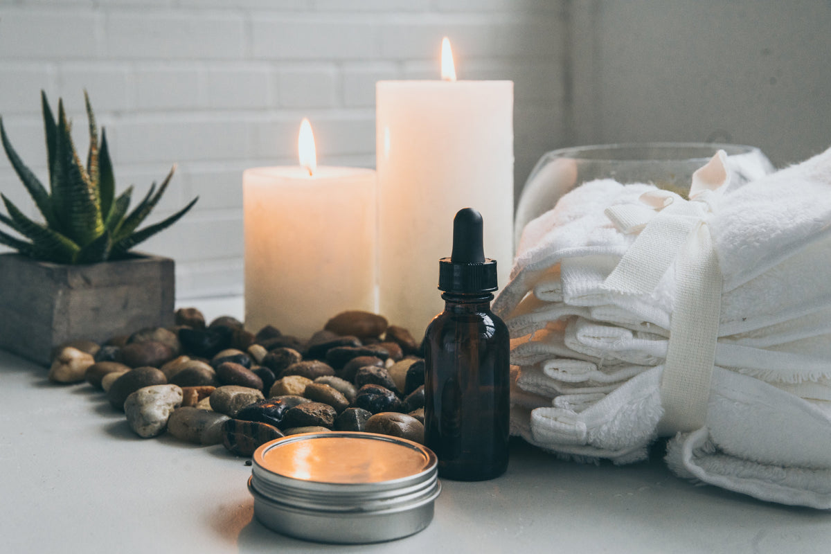 Candles, essential oil bottle, and towels on a table with a plant in the background